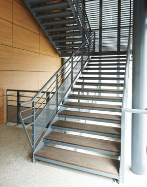 Escalier en acier laqué, marches en tôles pliées et bois avec garde corps composé d'une main courante, deux sous lisses et une partie basse en tôle perforée. Espace Pasteur Heyrieux
